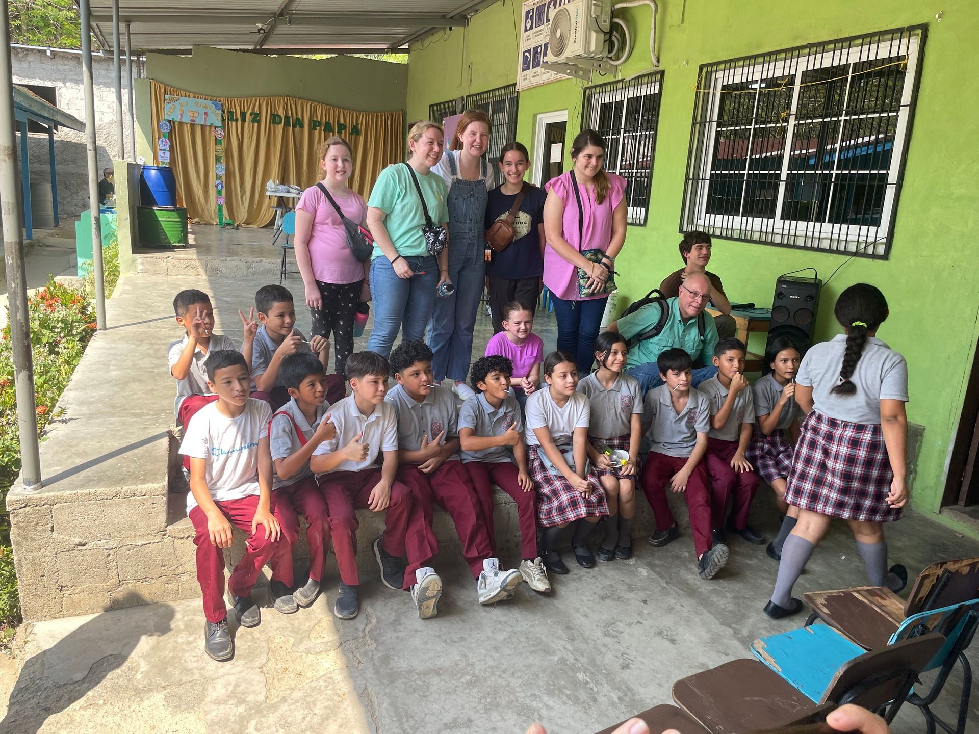 A group of children are posing for a picture in front of a green building.