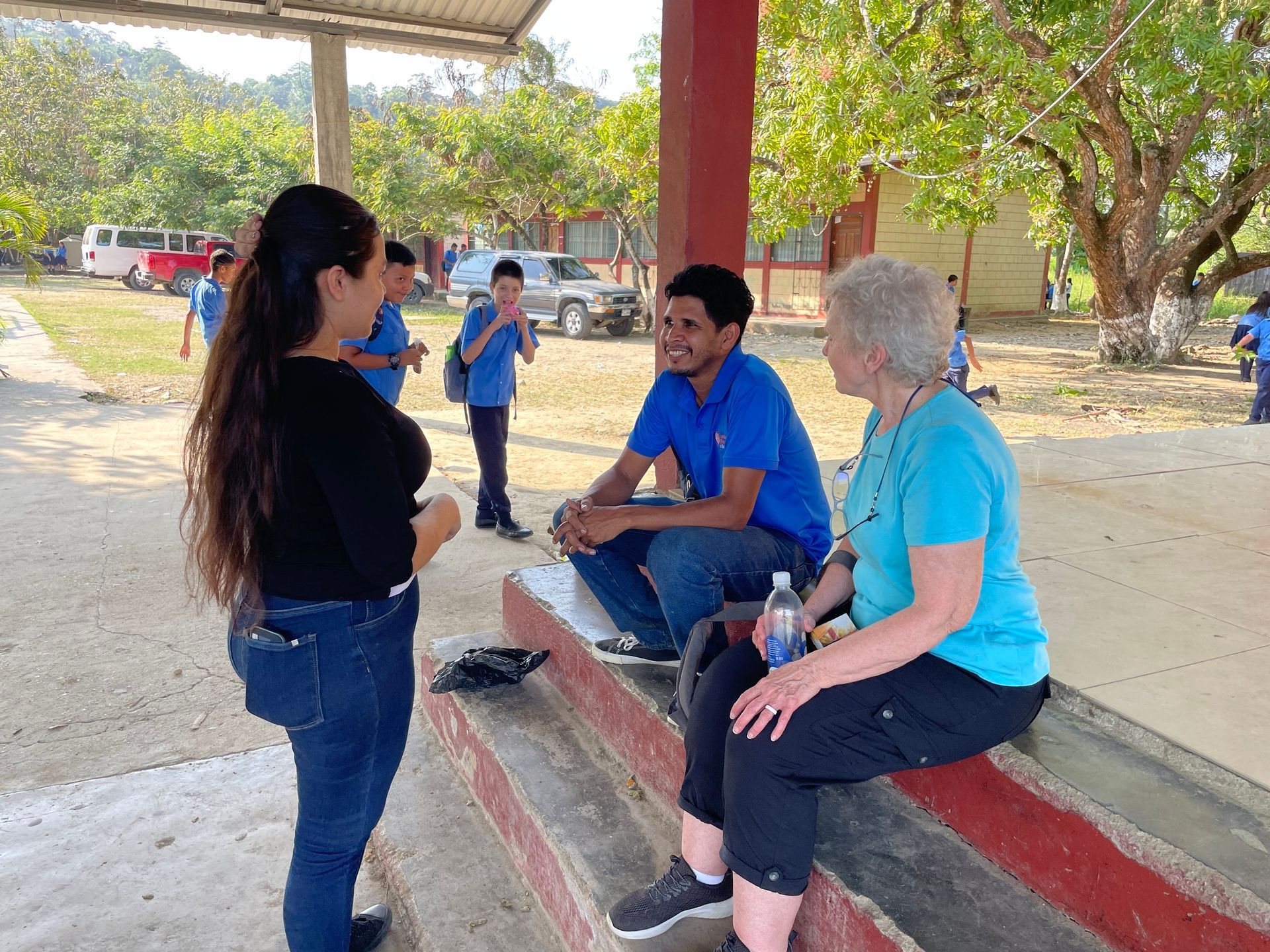A group of people are sitting on a bench talking to each other.