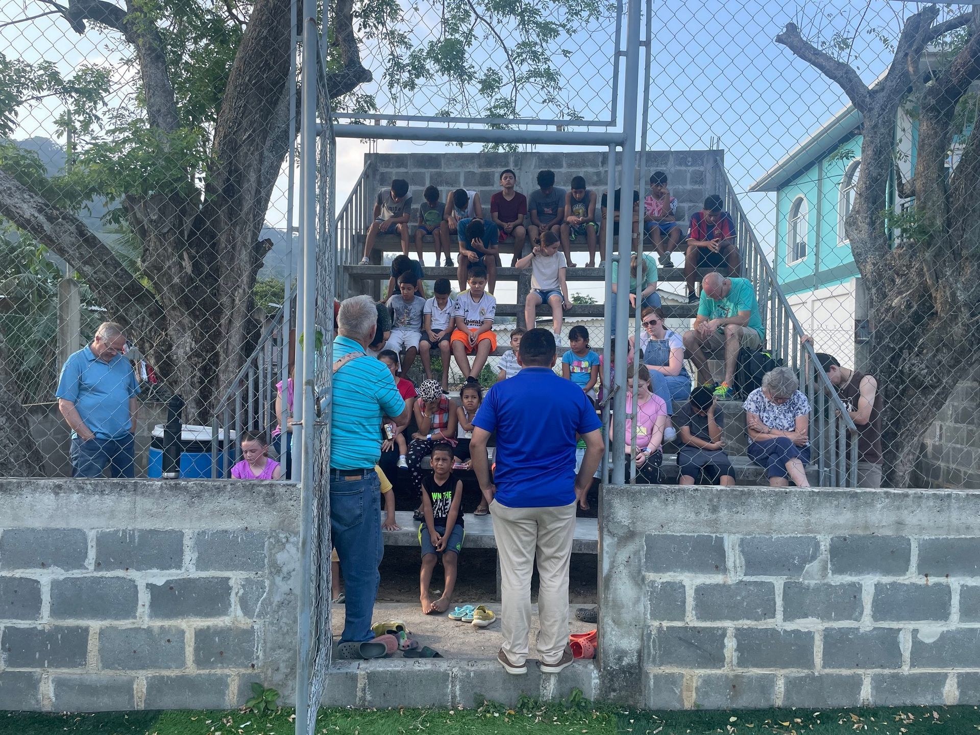 A group of people are sitting on bleachers behind a chain link fence.