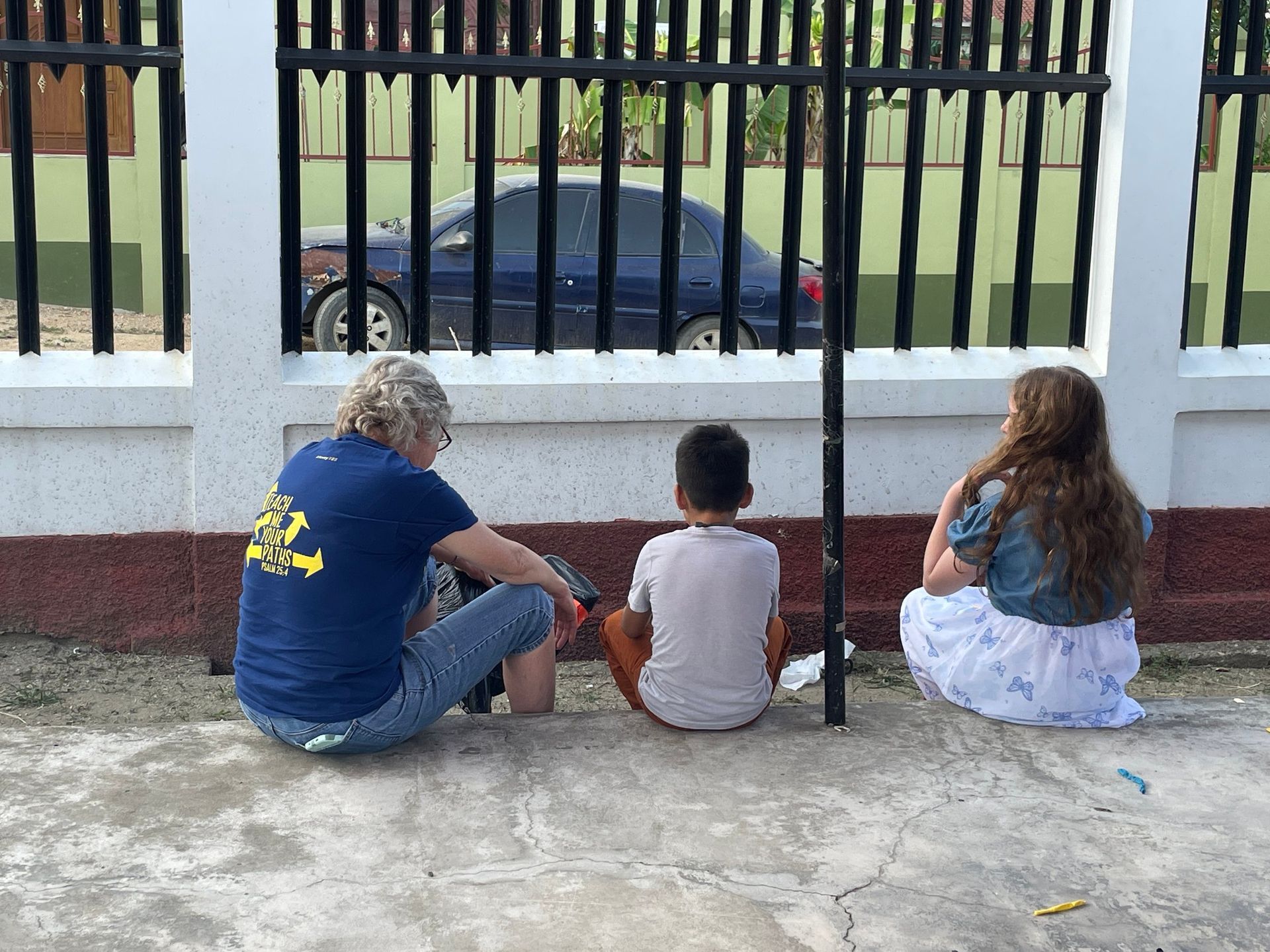 A man in a blue shirt that says ' i love you ' on it sits on the ground with two children