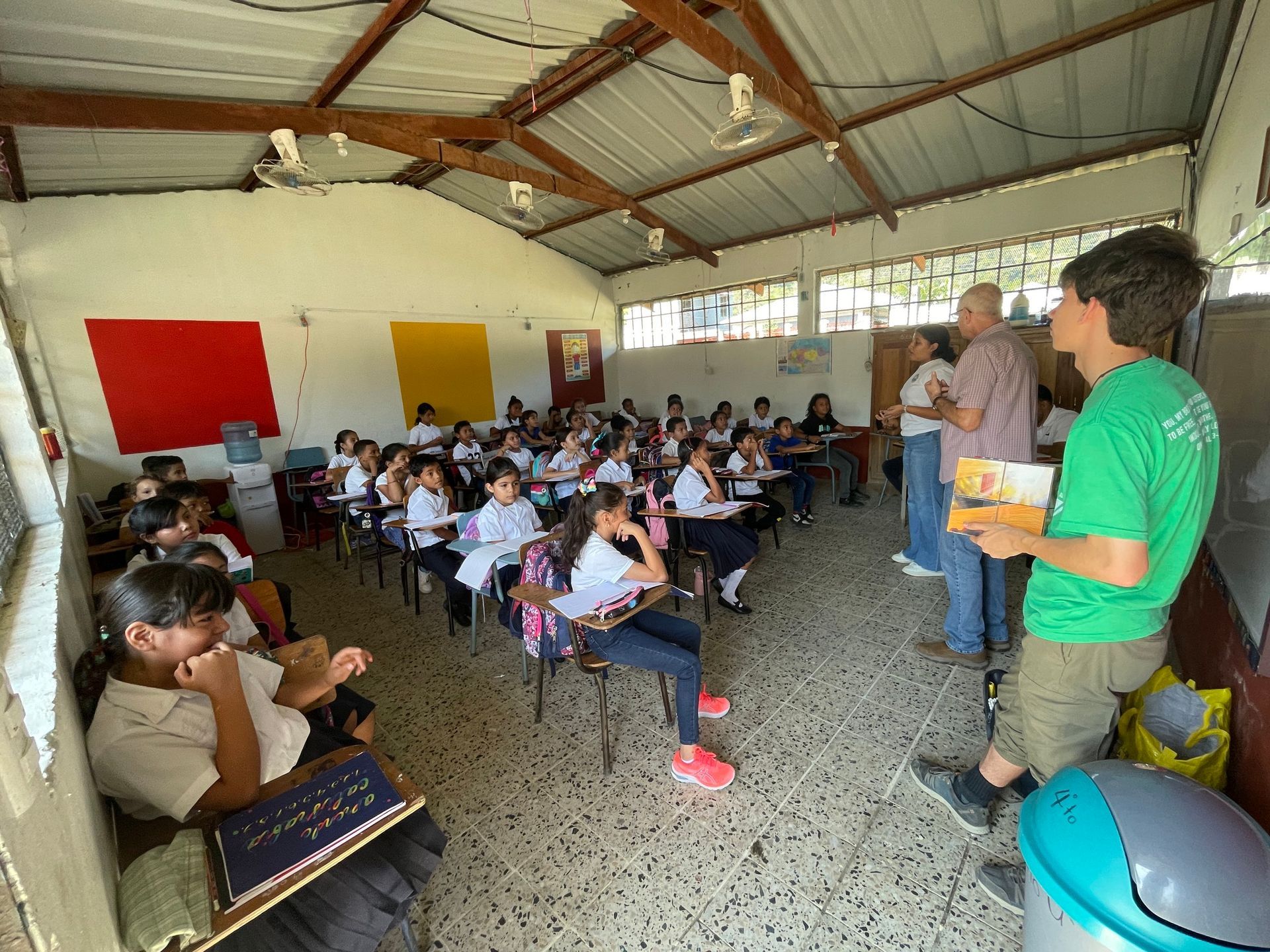 A man in a green shirt is standing in front of a classroom full of children.