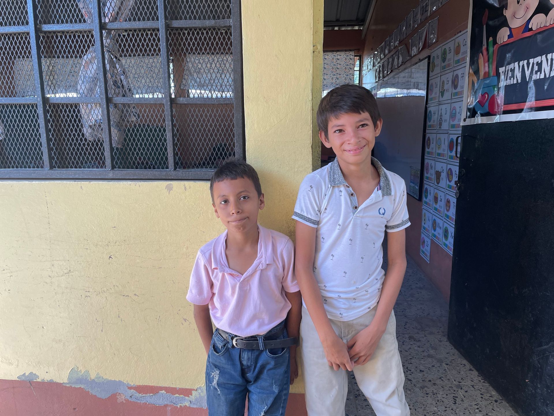 Two young boys are standing next to each other in front of a yellow building.