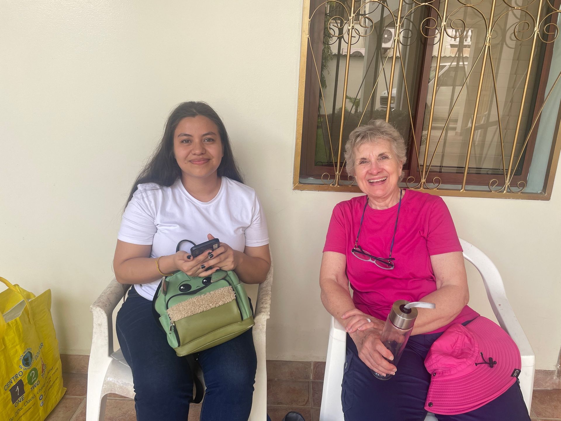 Two women are sitting in chairs in front of a window.