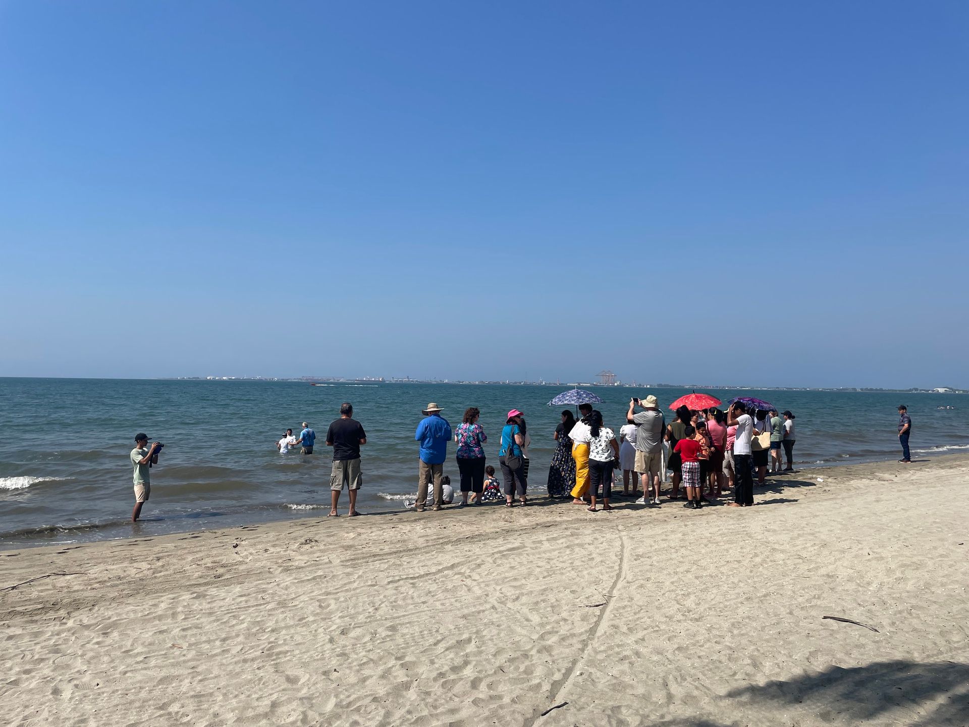 A group of people are standing on a beach looking at the ocean.
