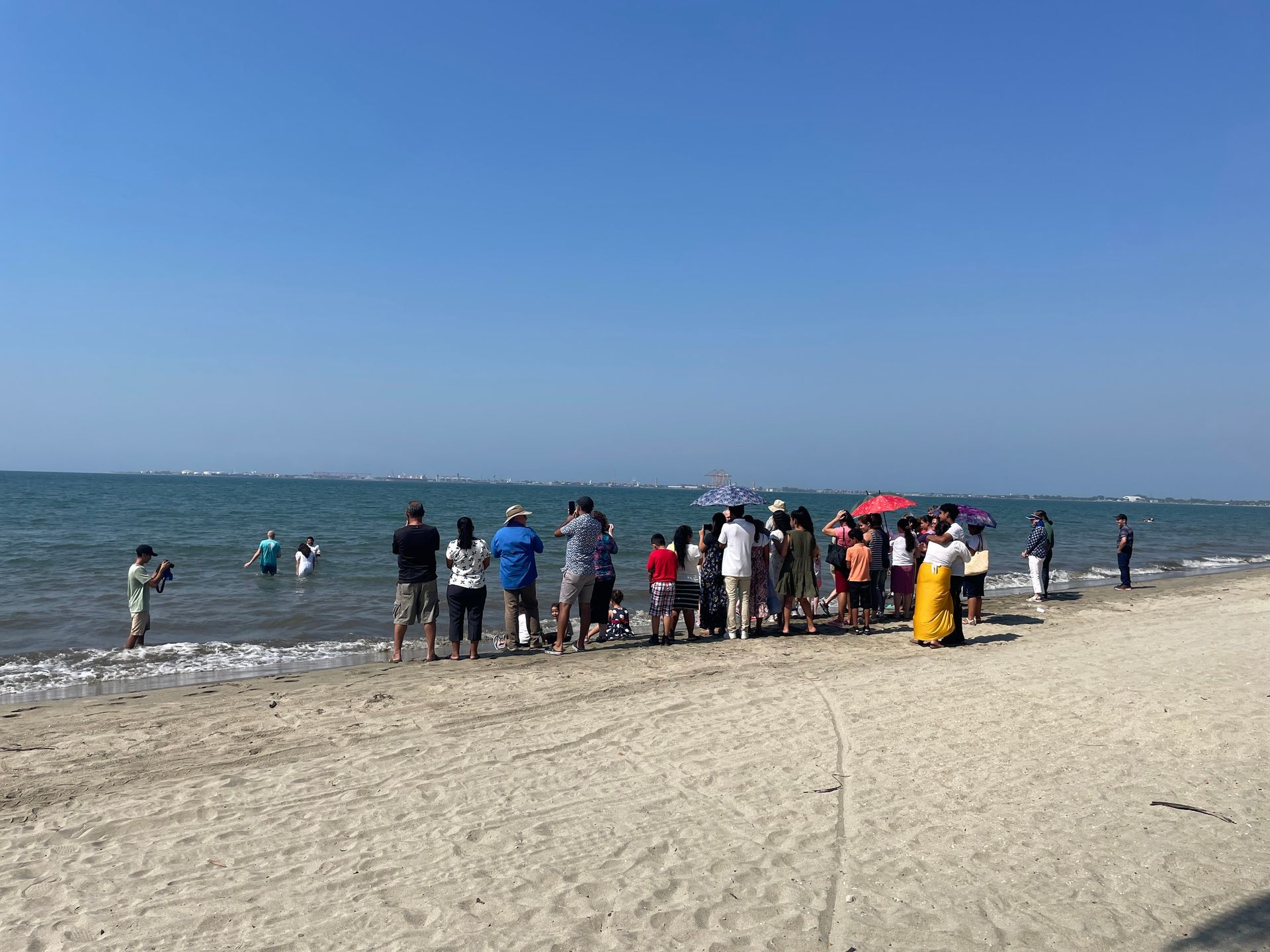 A group of people are standing on a beach looking at the ocean.