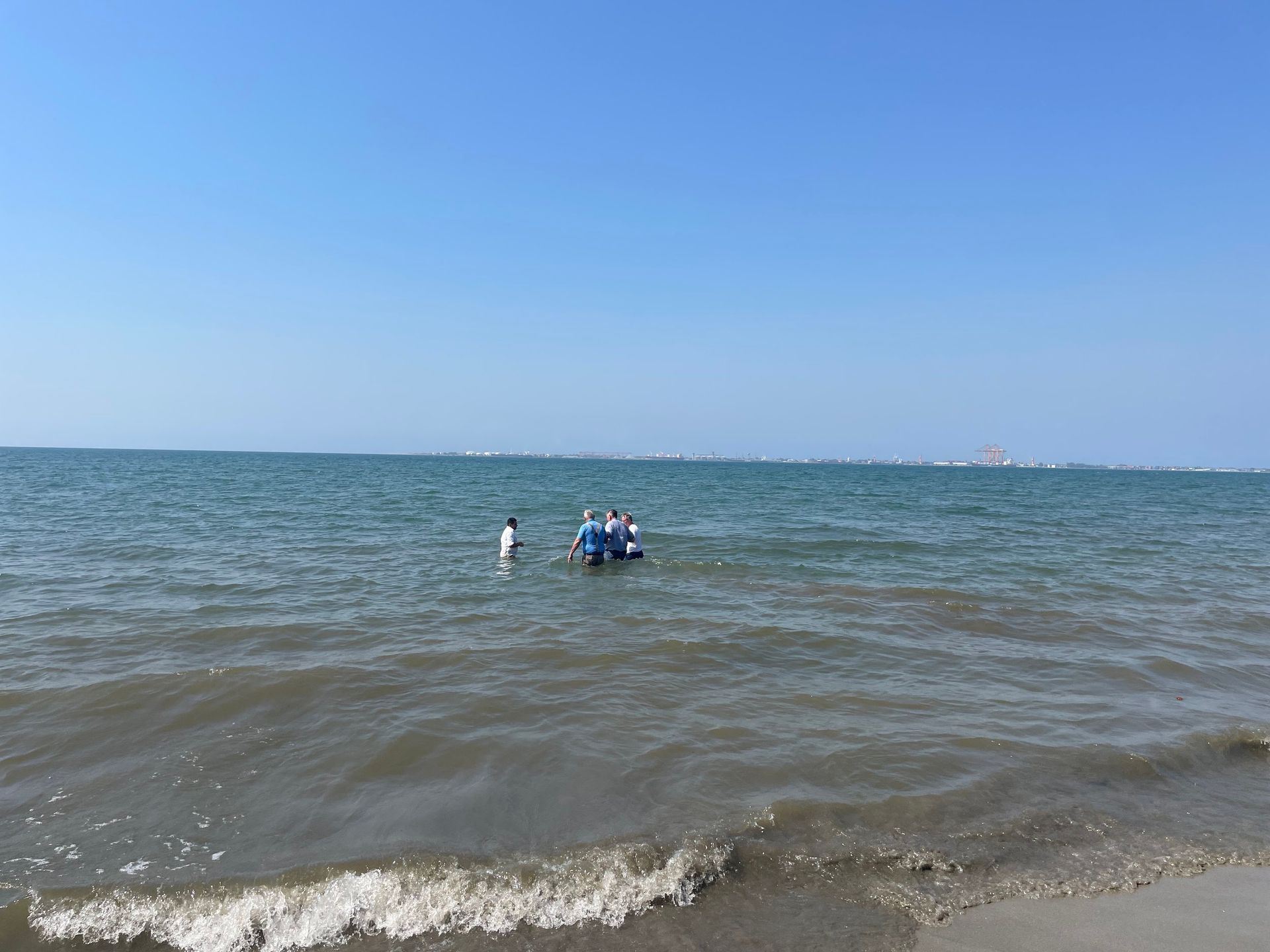 A group of people are standing in the water on a beach.