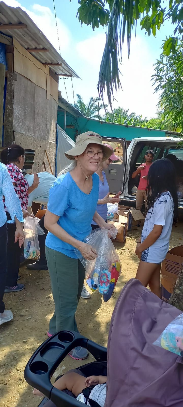 A woman in a hat is standing in front of a van holding a bag of food.