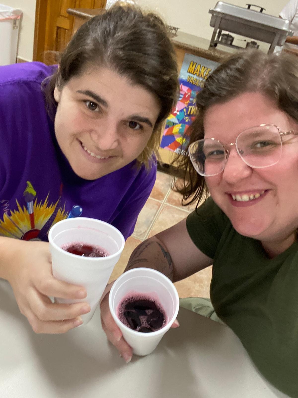 Two women are sitting at a table holding cups of wine