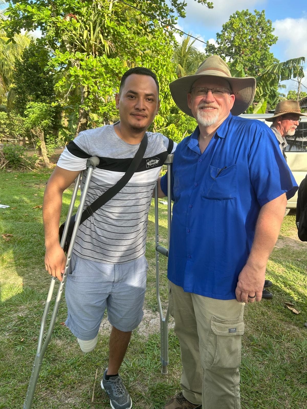 A man with a prosthetic leg is standing next to another man with crutches.