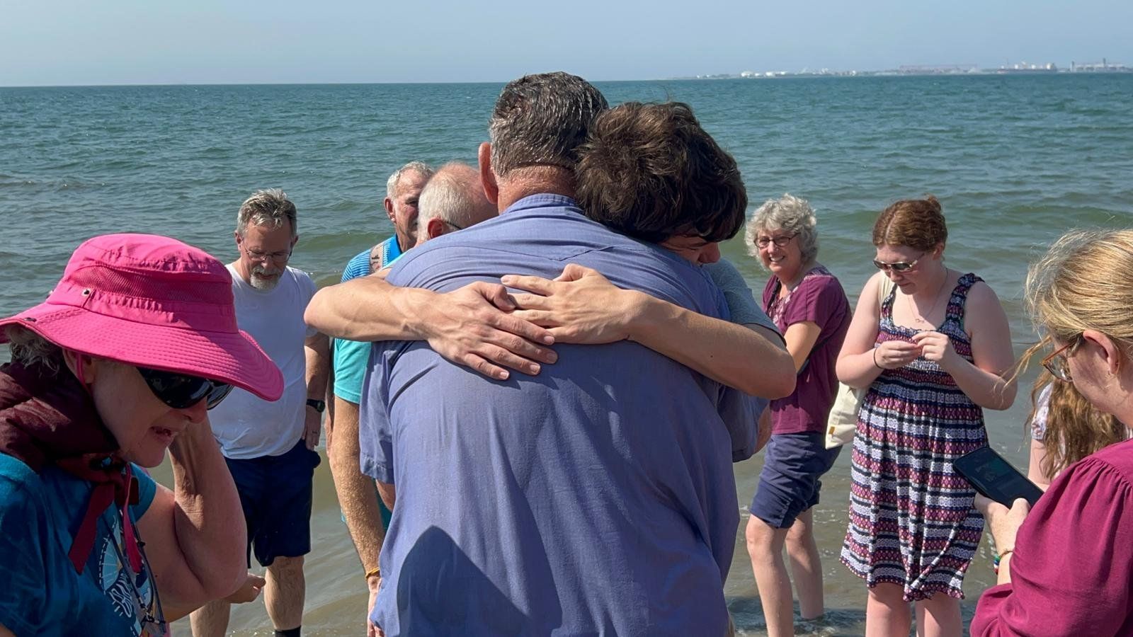 A group of people are hugging each other on the beach.