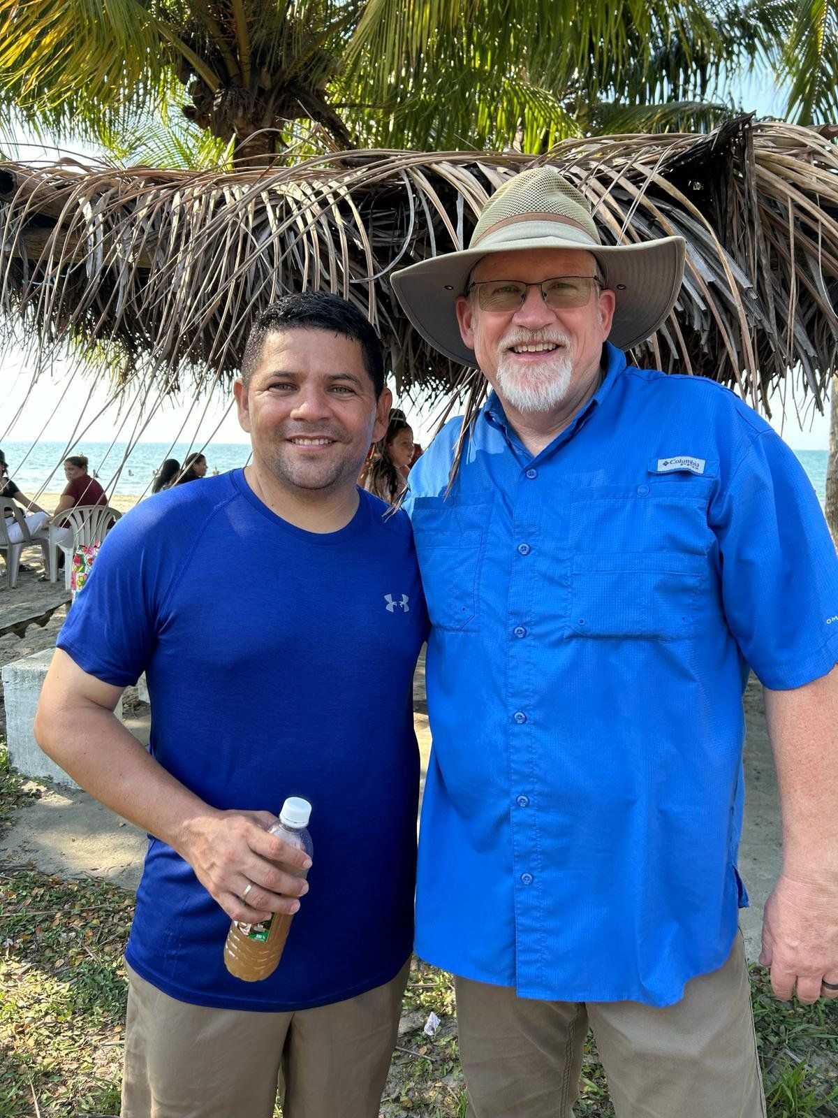 Two men are posing for a picture in front of a palm tree.