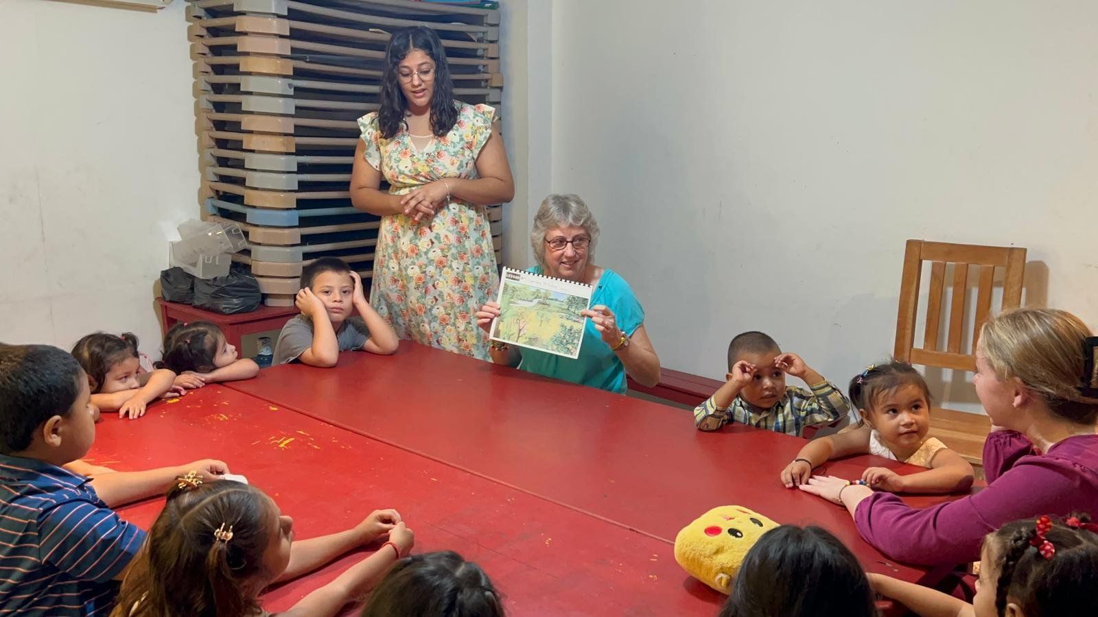 A woman is reading a book to a group of children sitting around a table.