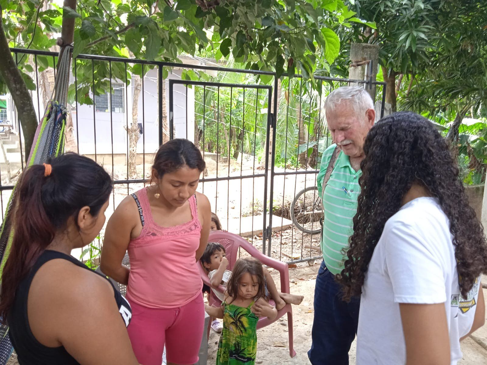 A group of people are standing in front of a fence talking to each other.