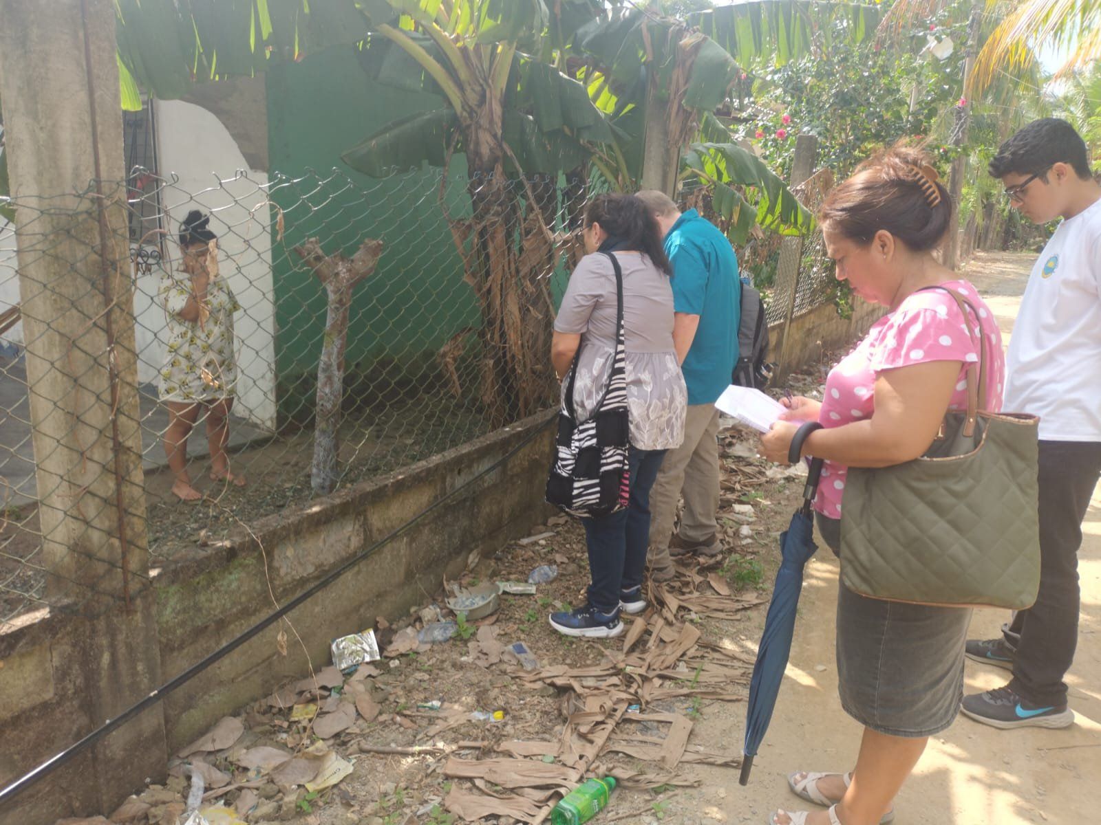 A group of people are standing in front of a chain link fence.