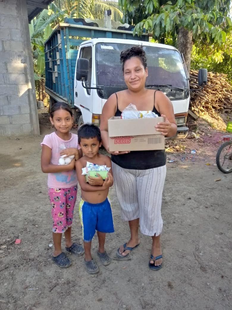 A woman and two children are standing in front of a truck holding boxes.