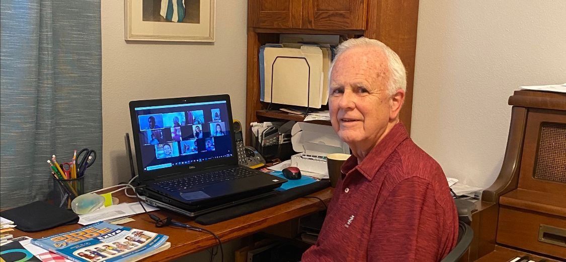 A man is sitting at a desk in front of a laptop computer.