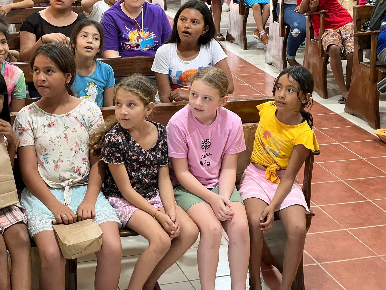 A group of young girls are sitting on a bench in a church.