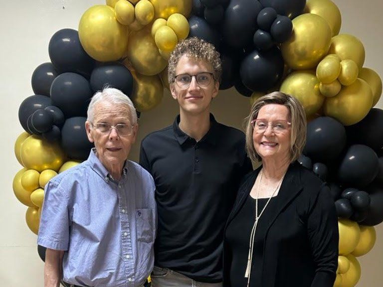 A man , a woman and a boy are posing for a picture in front of balloons.