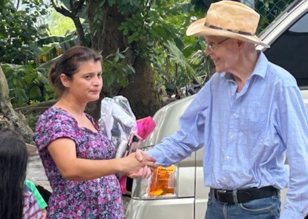 A man in a straw hat shakes hands with a woman in a purple dress.