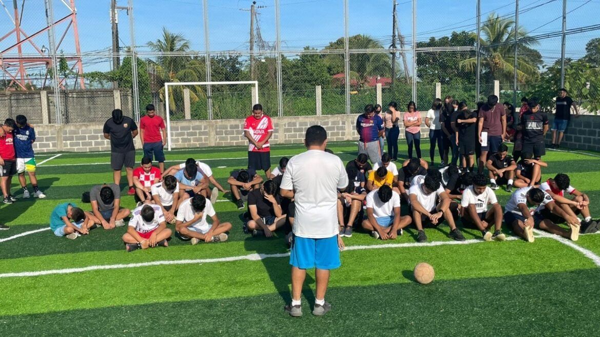 A man is standing in front of a group of people sitting on a soccer field.