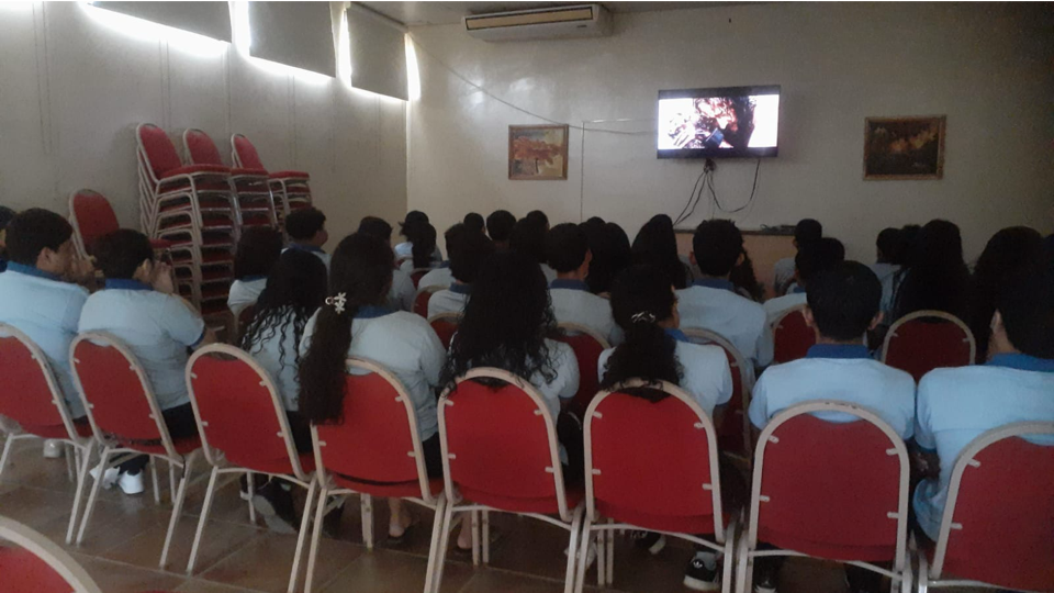 A group of people are sitting in red chairs in front of a television