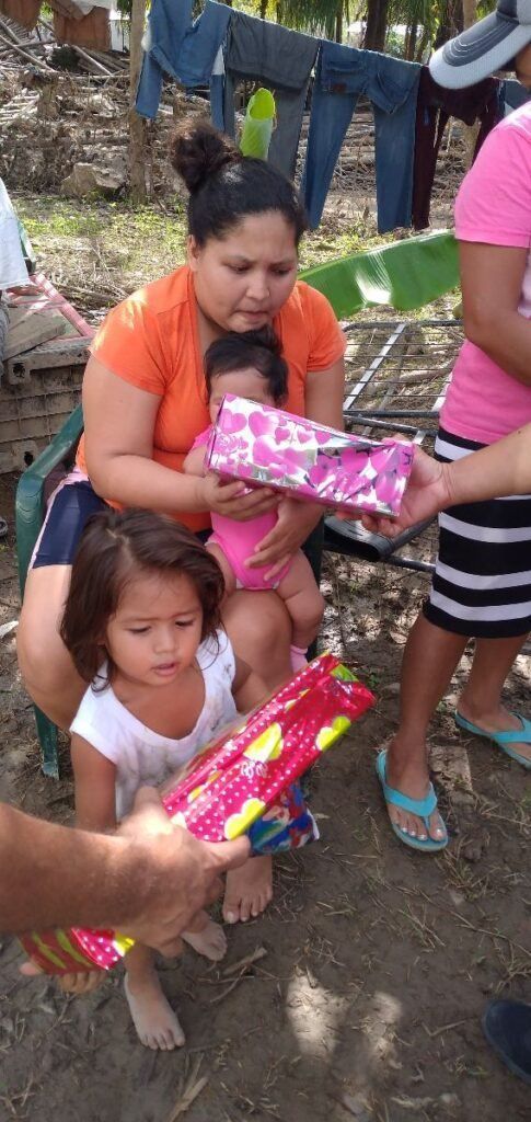 A woman is holding a baby and giving a gift to another woman.
