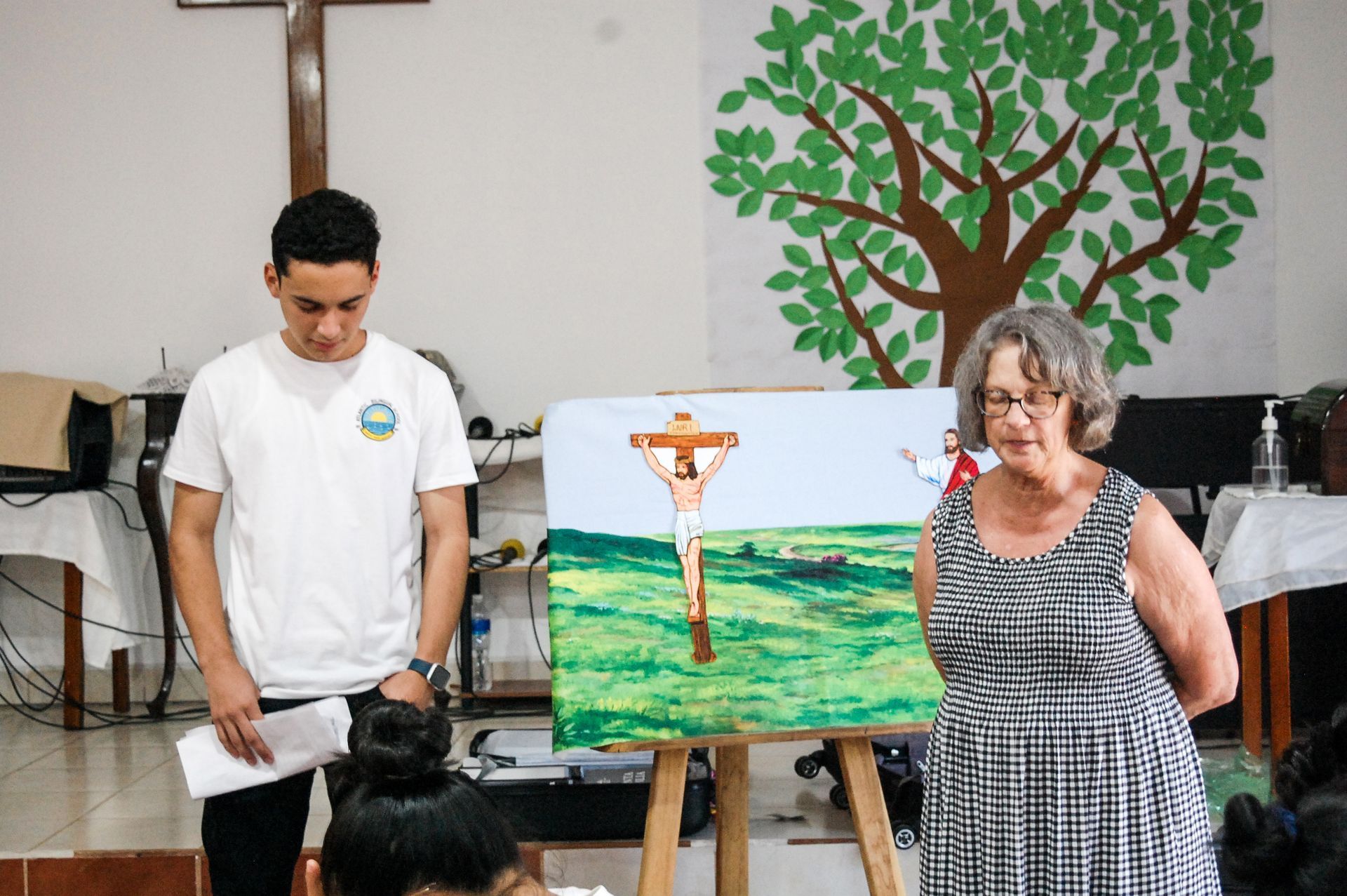 A man and a woman are standing in front of a painting of jesus on the cross.