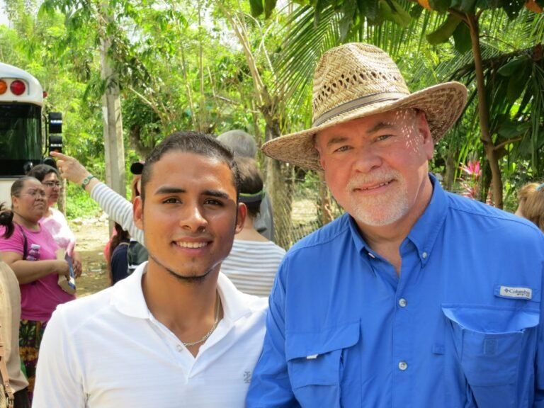 A man wearing a straw hat is standing next to another man in a blue shirt.