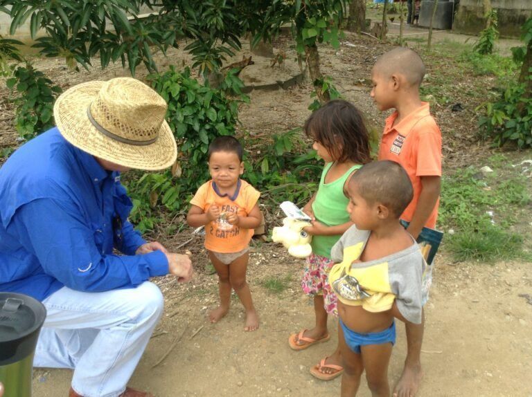 A man wearing a straw hat talks to a group of children