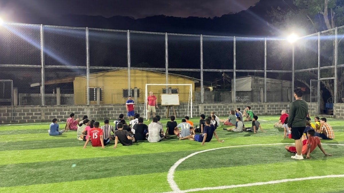A group of people are sitting on top of a soccer field at night.