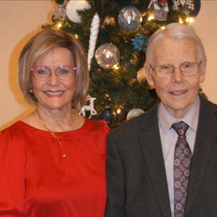 A man and woman are posing in front of a christmas tree
