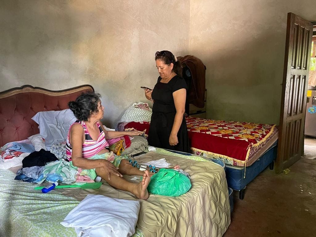 A woman is standing next to a woman sitting on a bed.