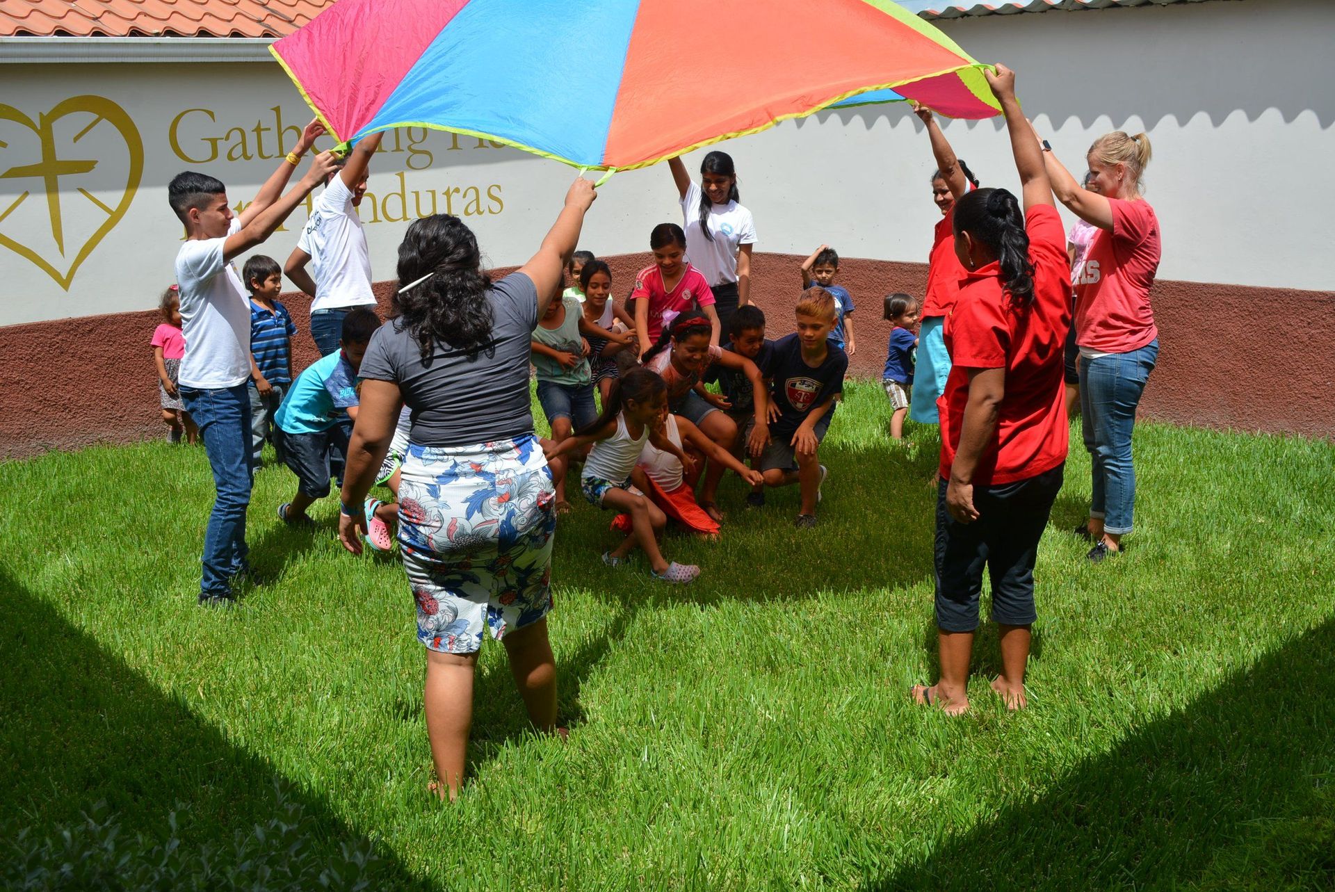 A group of people are playing with a colorful parachute in the grass.