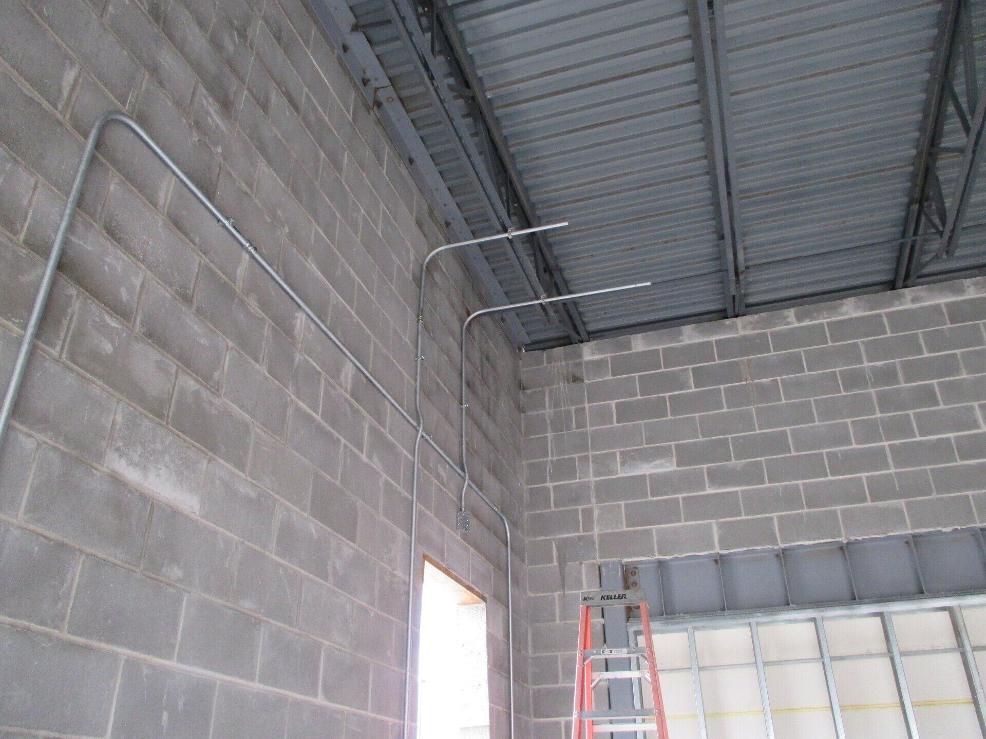 Electrical conduit runs along a concrete block wall, near a window and metal roof.