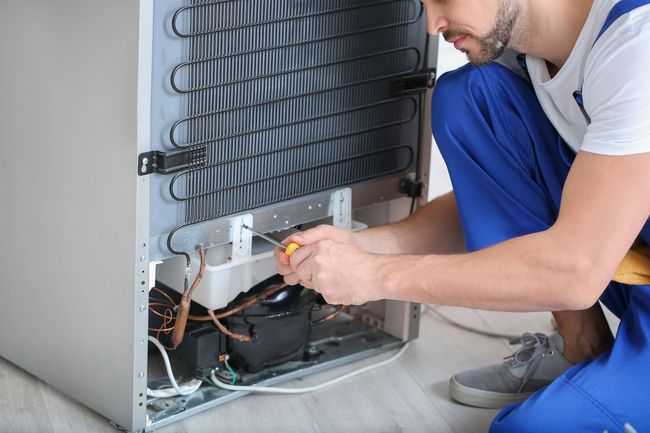 A man is fixing a refrigerator with a screwdriver.