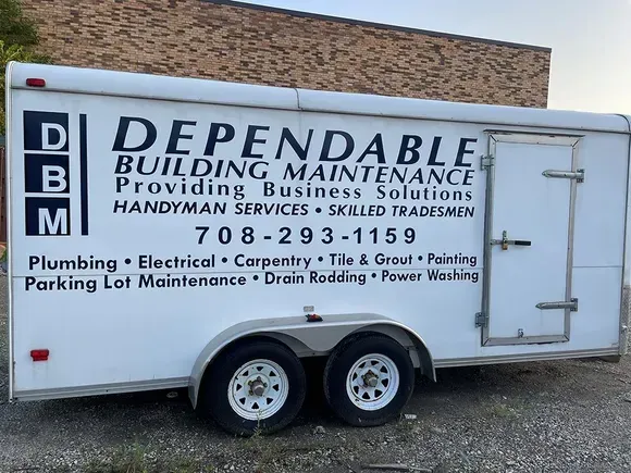 A trailer for dependable building maintenance is parked in front of a building