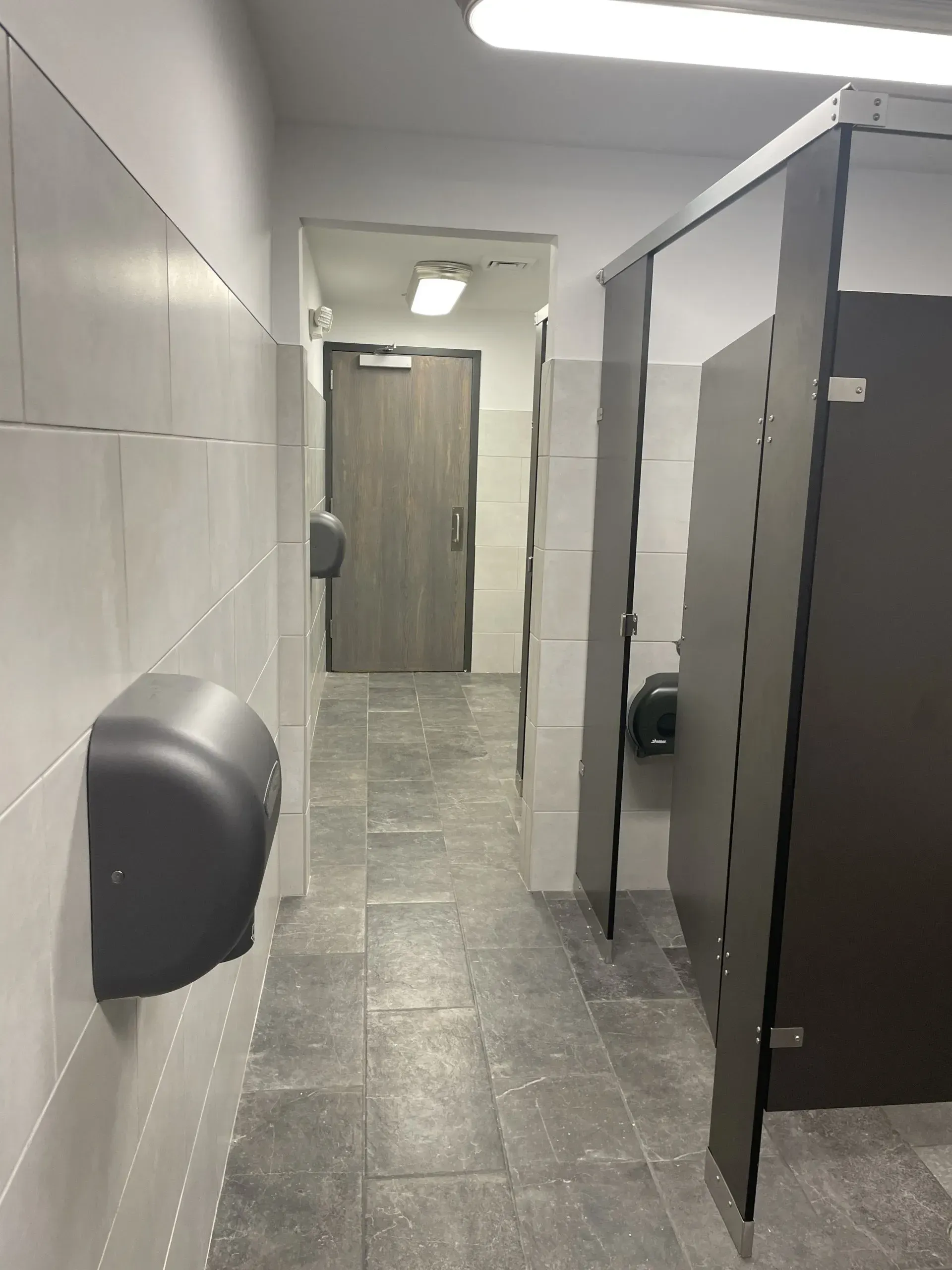 A hallway in a public restroom with a hand dryer on the wall.
