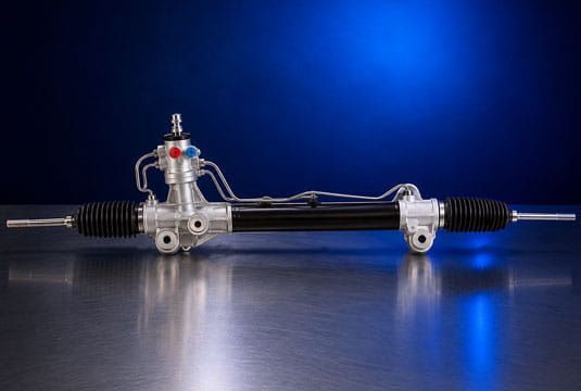 Conjunto de cremallera de dirección automotriz sobre una superficie reflectante azul, iluminada contra un fondo azul oscuro.