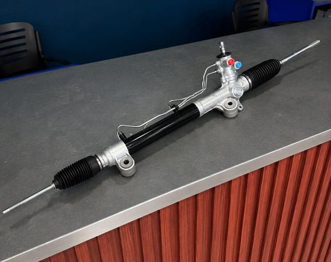 Conjunto de cremallera de dirección automotriz con fuelles negros sobre un mostrador.