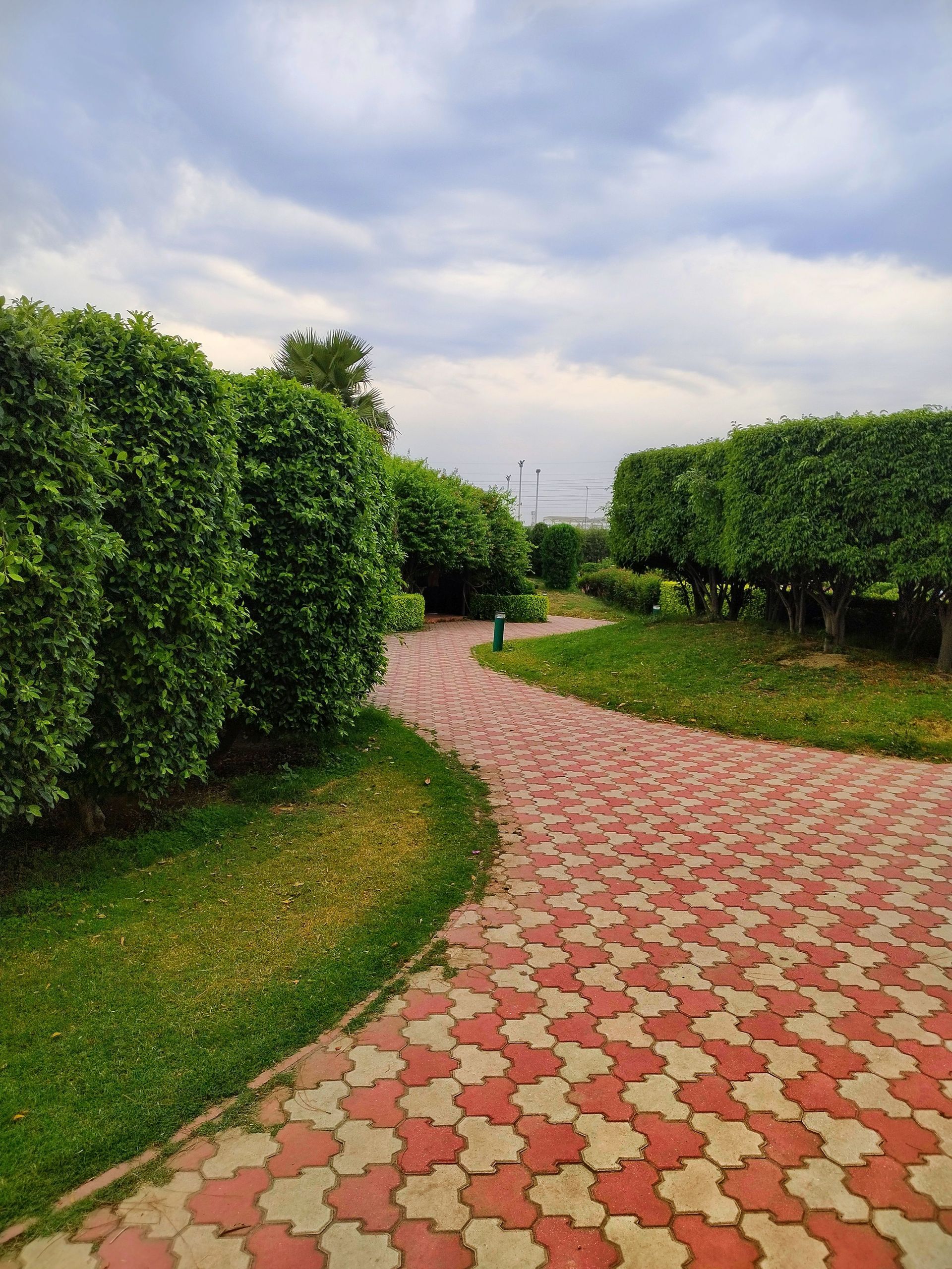 Curving red-and-cream brick path through a green park under a cloudy sky