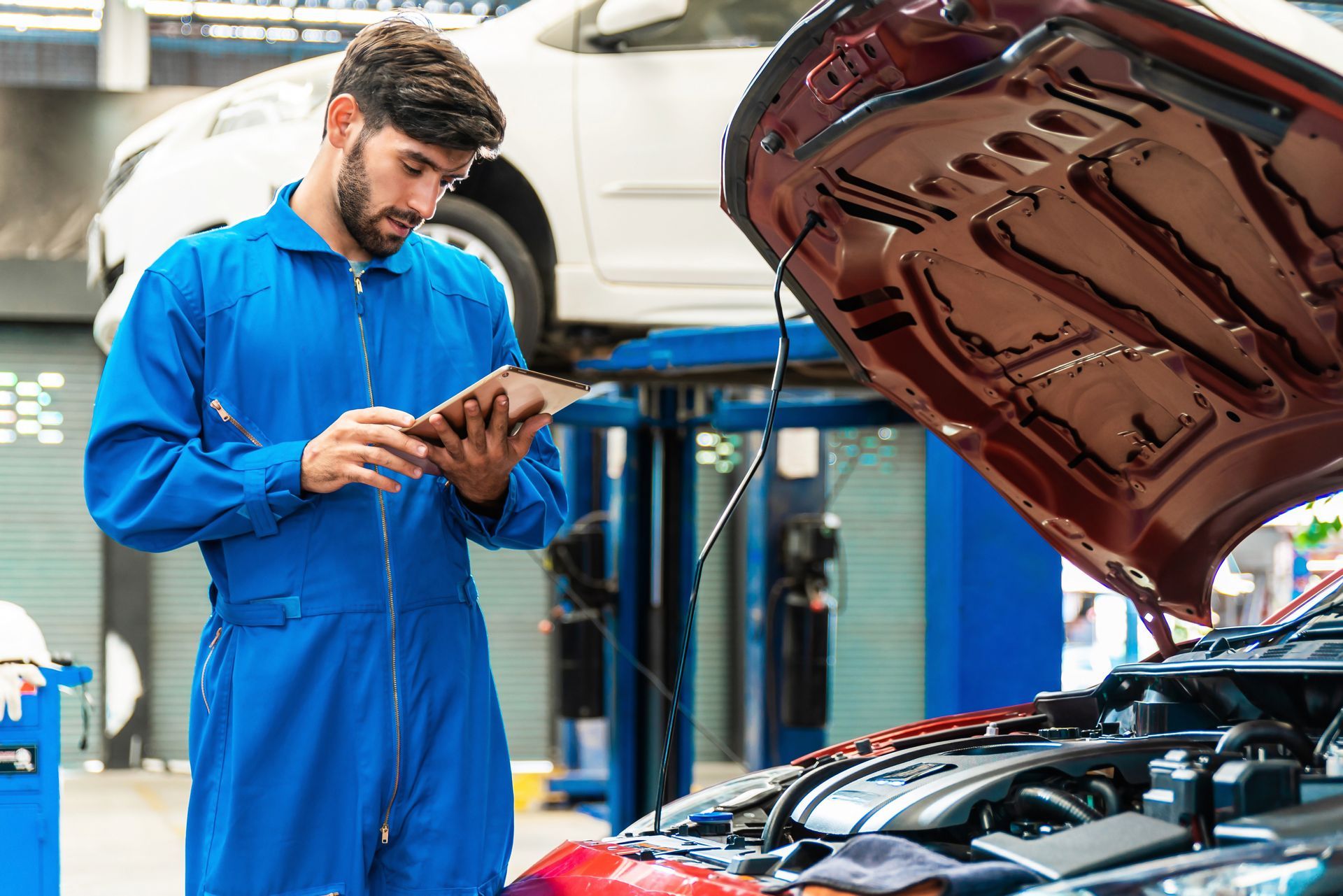 A mechanic is looking at a tablet while working on a car in a garage.