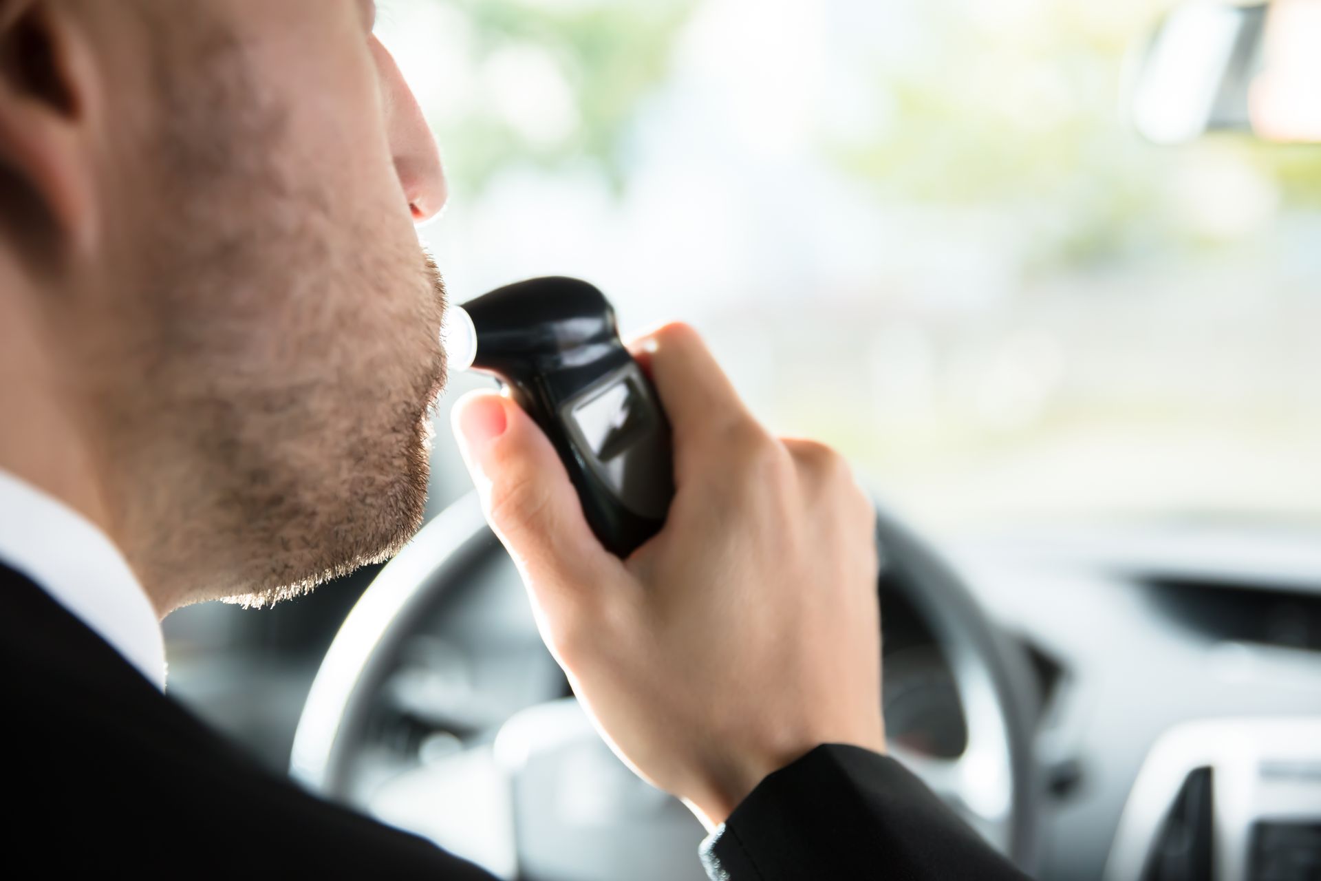 A man in a suit is talking on a walkie talkie while driving a car.