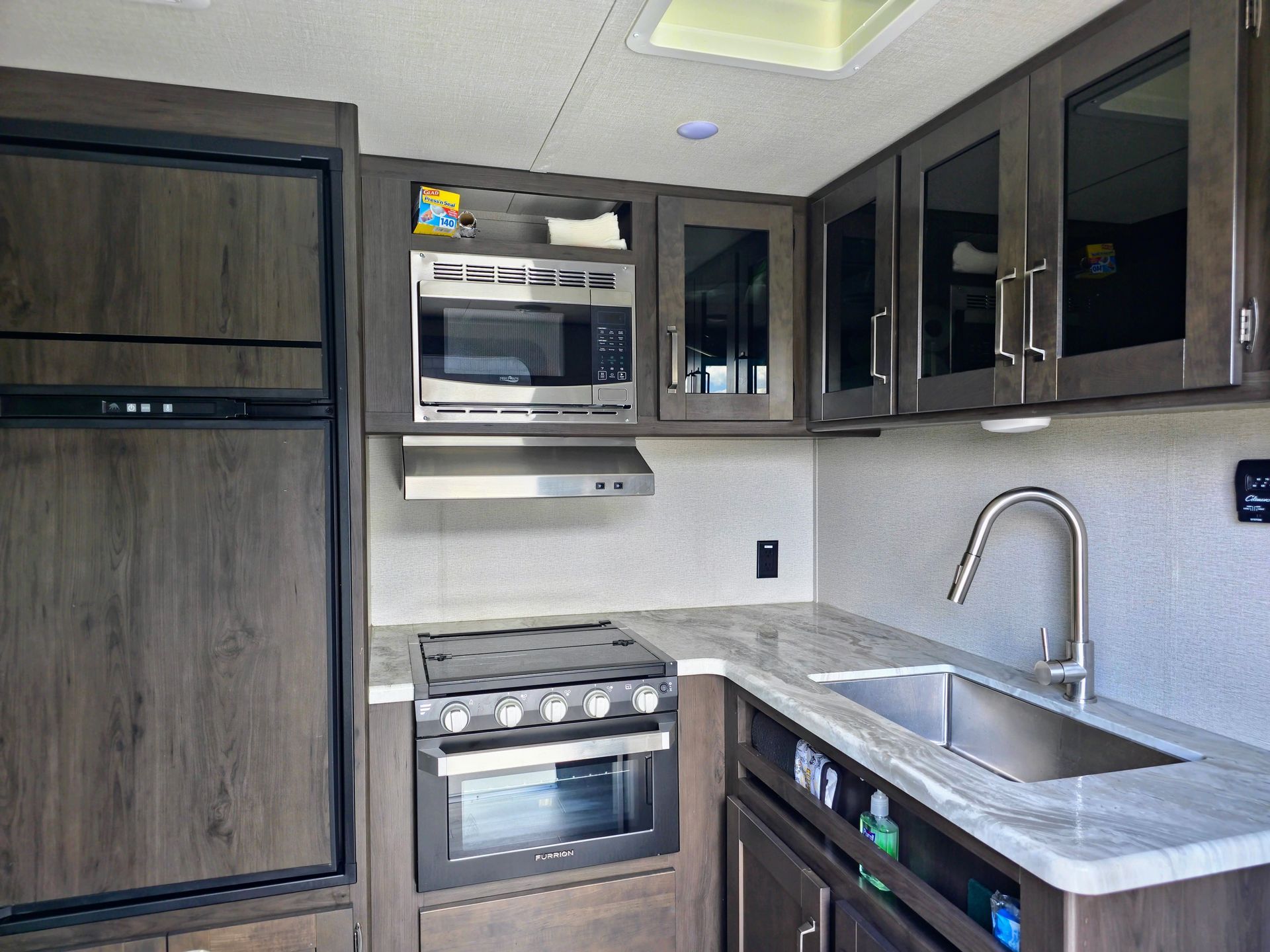 Modern kitchen with stainless steel appliances, dark cabinets, gray countertops, and a sink by the window.