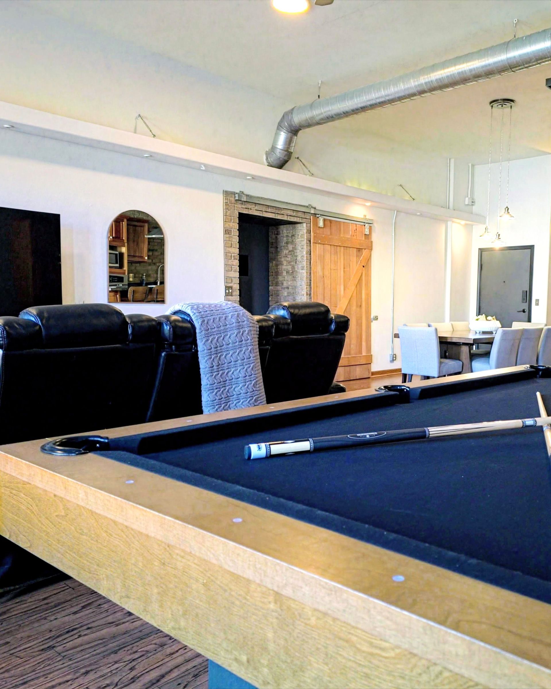 Pool table in a basement lounge with black couches, wood paneling, and exposed ductwork.