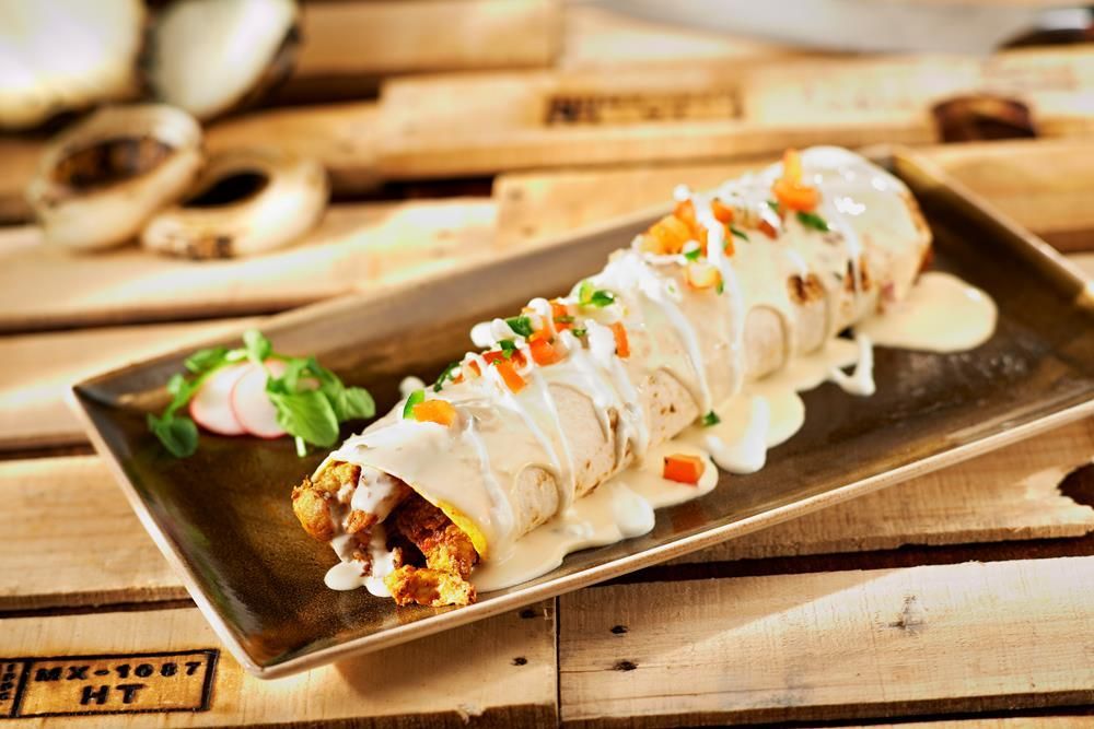 Sushi roll drizzled with creamy sauce on a rectangular plate, garnished with herbs and orange roe