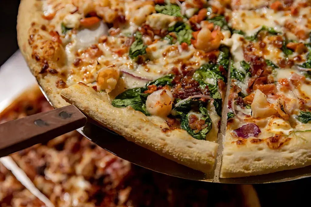 Two pizzas on wooden peels, topped with shrimp, greens, and melted cheese