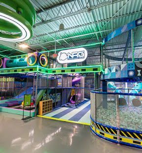 Colorful indoor obstacle play area with neon lights, netted tunnels, ramps, and a ball pit under a metal سقف