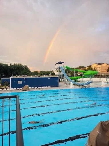 Outdoor swimming pool with a rainbow over the water and slide in the background