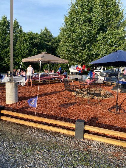 Outdoor patio with tables, umbrellas, and people at a mulch-covered garden area on a sunny day
