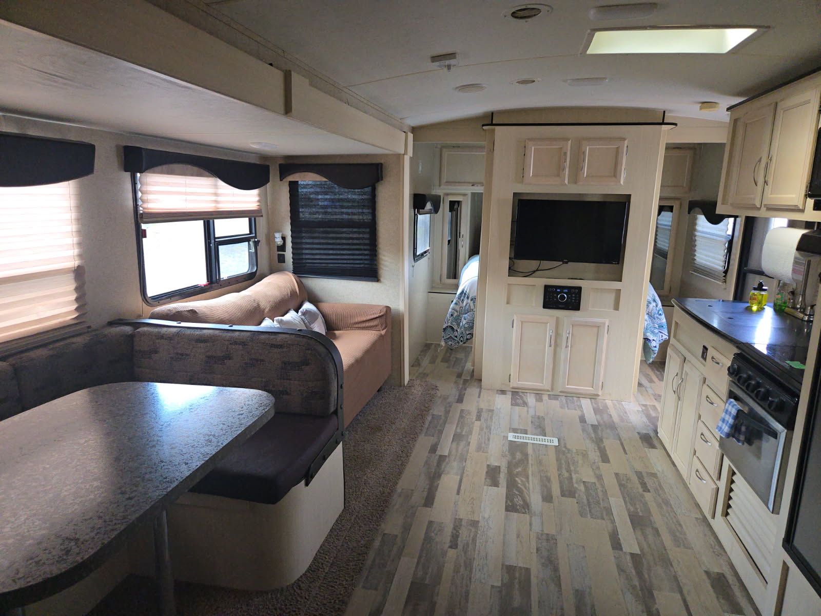 Interior of a modern RV kitchen and living area with beige cabinetry, dark counters, and a sofa by the window.